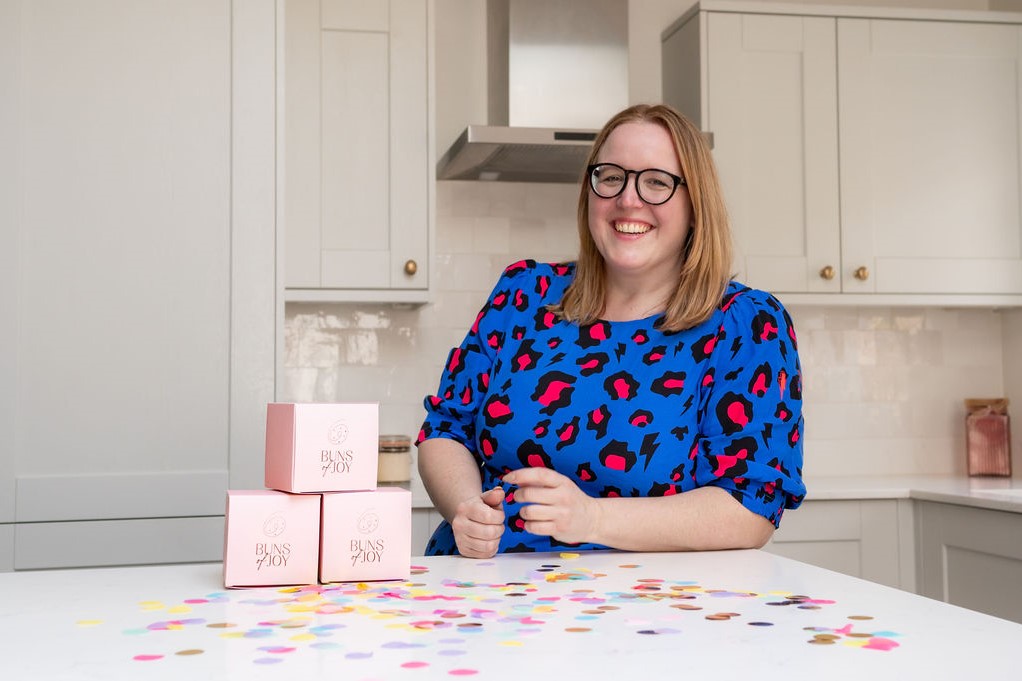 image of Leah smiling next to 3 individual pink bun boxes stacked up