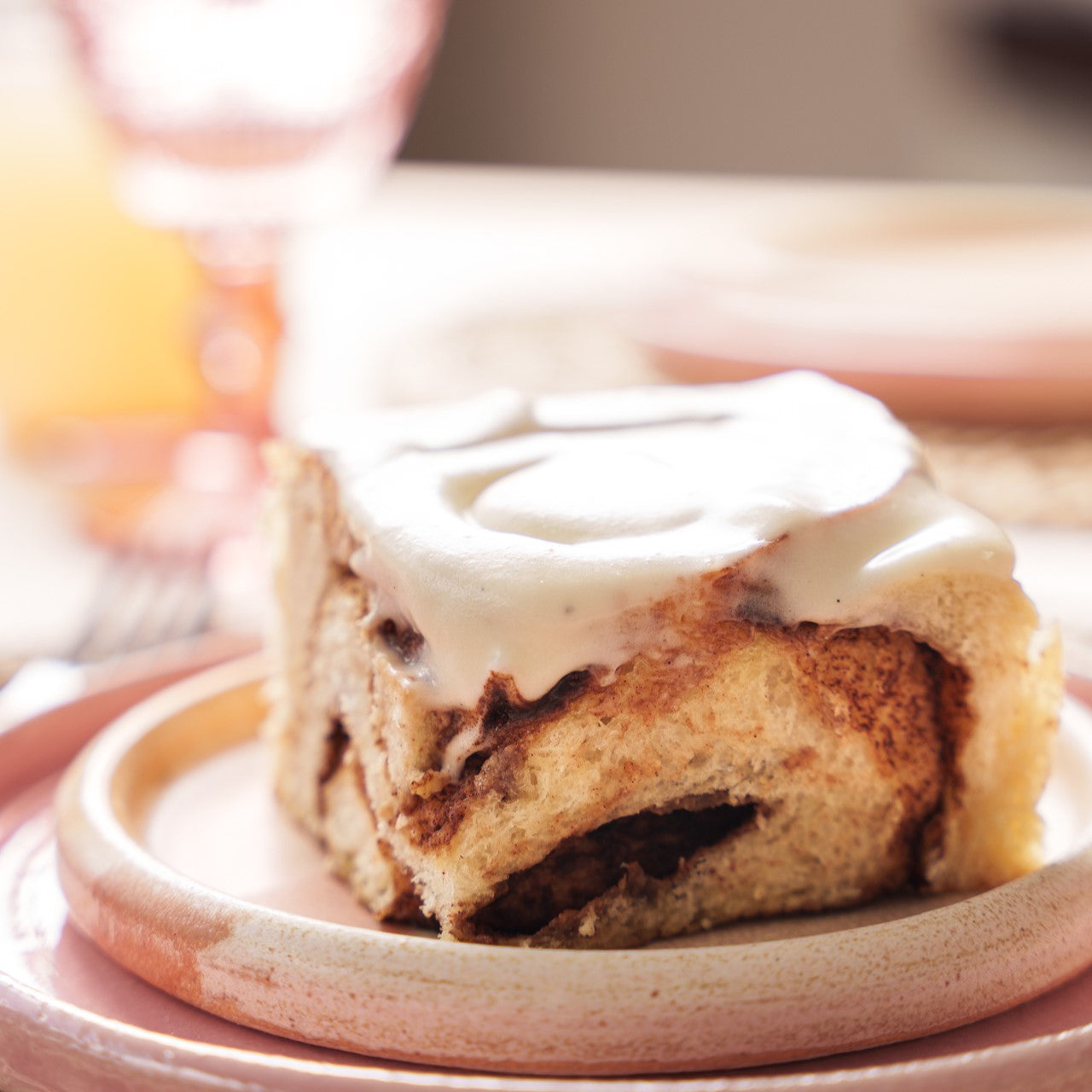 cinnamon bun on a ceramic plate with the cream cheese frosting glistening