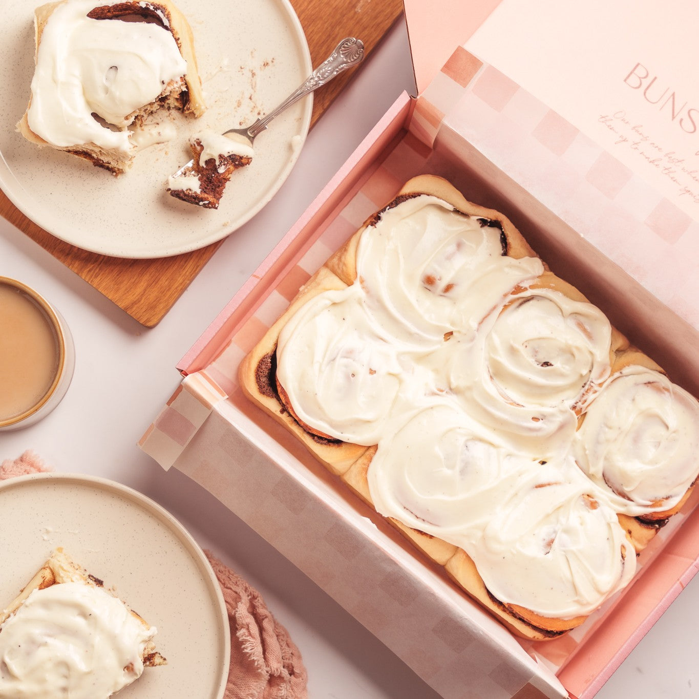 a box of 6 cinnamon buns in a buns of joy gift box, next to buns onf a plate being eaten