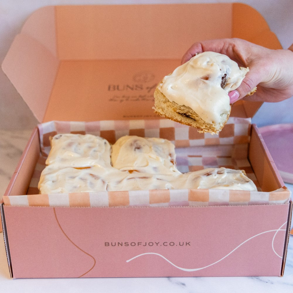 a hand taking a cinnamon bun out of a gift box with 6 cinnamon buns inside