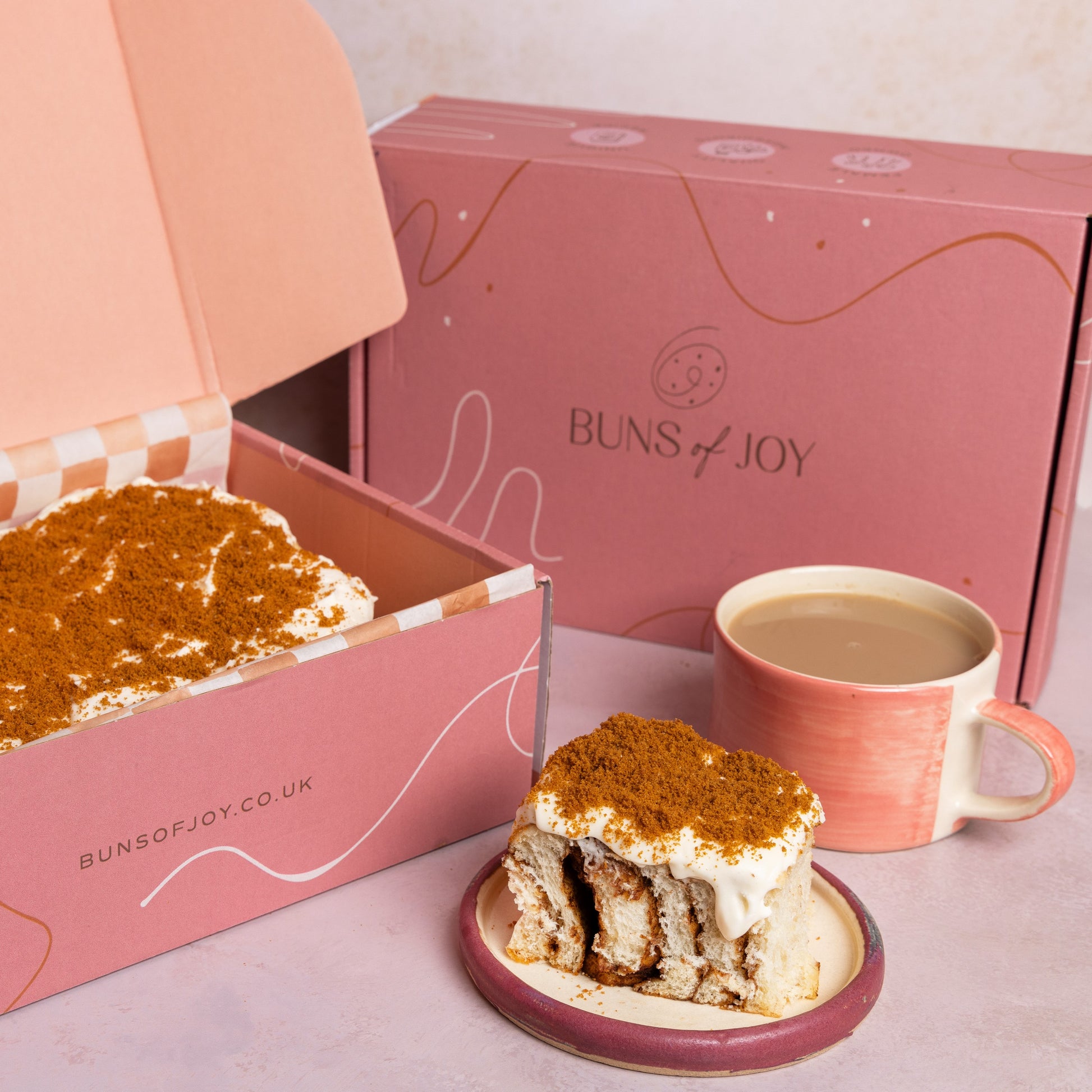 Biscoff Buns next to a pink Buns of Joy gift box and a cup of tea